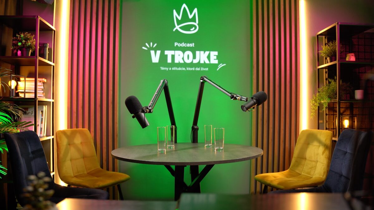 Moderné variabilné podcastové štúdio s dvoma mikrofónmi, stolom, stoličkami, svetelným logom a dekoráciou. Podcastové štúdio Bratislava – profesionálne nahrávanie