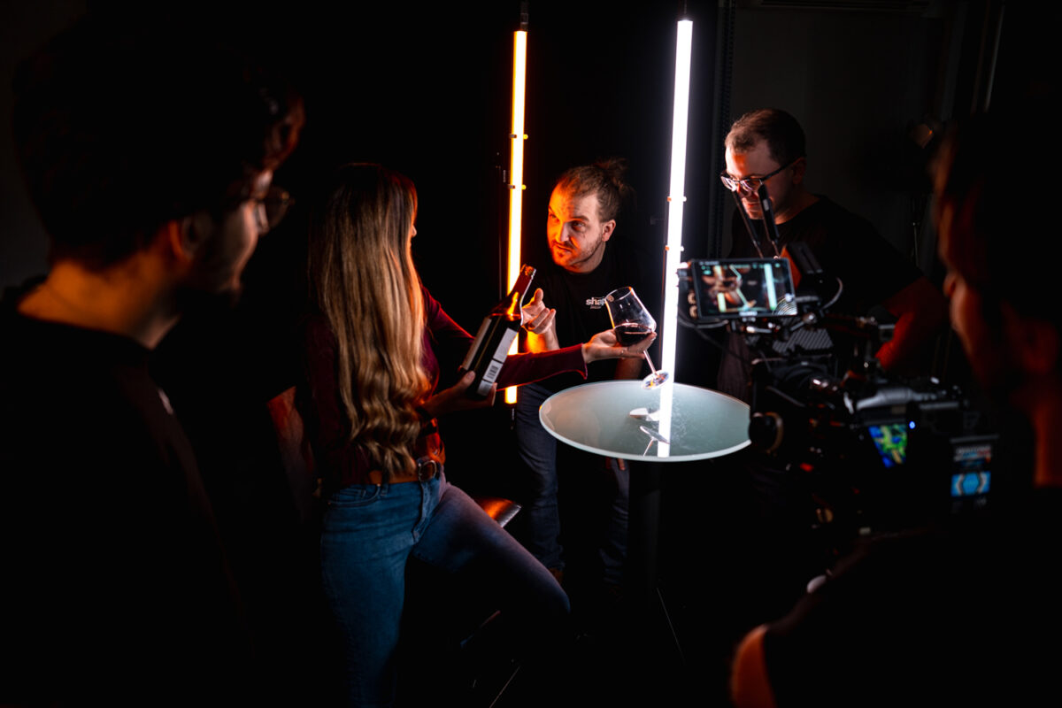 Režisér a filmový štáb počas nakrúcania reklamného produktového videa z produkcie SHAPE Production na scéne s pohárom vína a rotačným podstavcom.