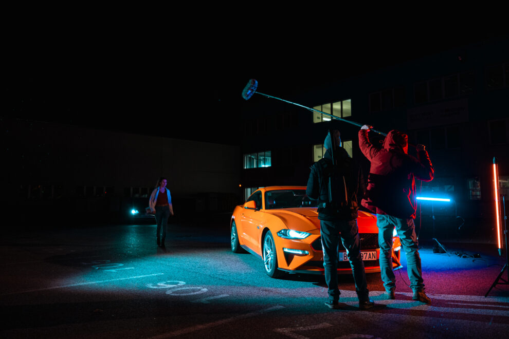 Kameraman a zvukár zaznamenajú farebne nesvietenú exteriérovú nočnú scénu s automobilom Mustang do reklamného spotu z dielne SHAPE Production.